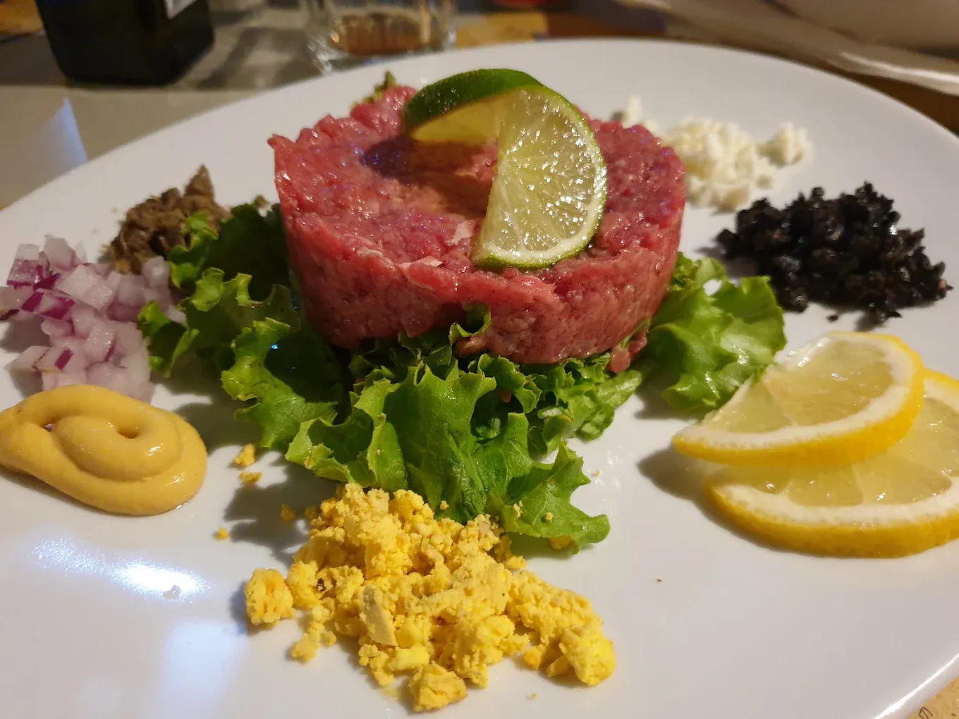 Tartare di Chianina con lime, cipolla rossa, olive e condimenti disposti attorno al piatto